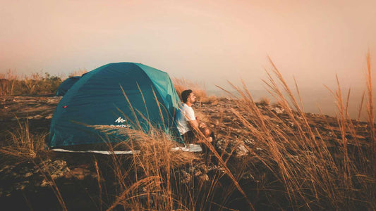 Man sat on the edge of his Blue tent on hillside relaxing in nature