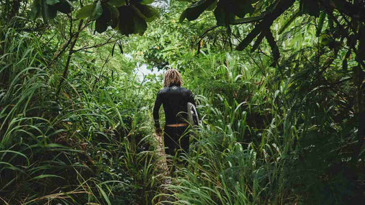 Man in wetsuit carrying surfboard through Jungle