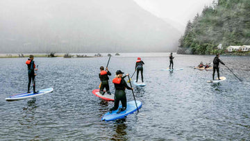 Group of paddle boarders on blue lake wearing life jackets surrounded by hills