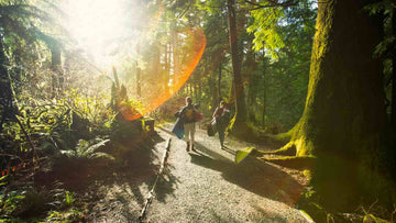 A couple walking through the woods carrying their water sports equipment