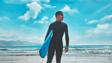 Person wearing Black wetsuit holding Paddle Board